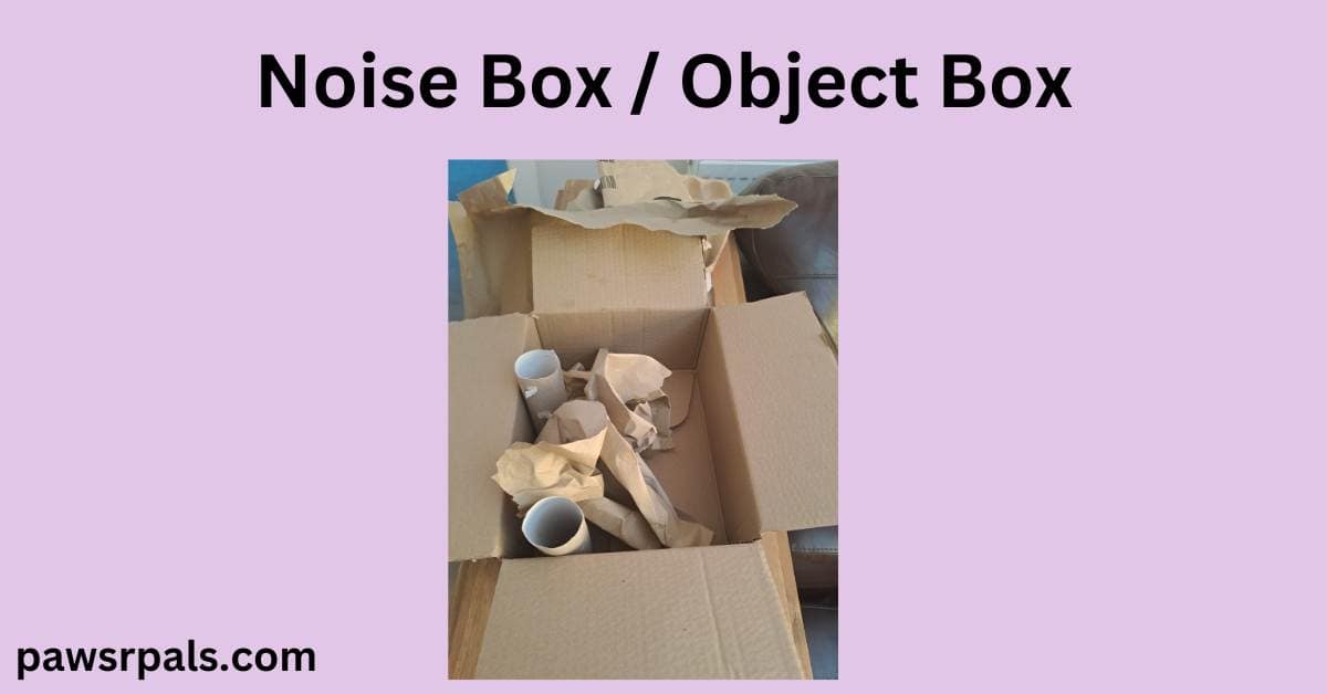 Noise box/ object box. Lilac background, image in the centre of an open cardboard box with some empty cardboard tubes and scrunched brown paper inside.