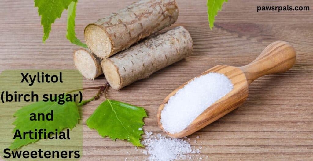 Xylitol (birch sugar) and Artificial Sweeteners. Image of three birch logs piled on top of each other, next to a long wooden scoop with white crystals on and in front of it